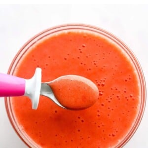 Steamed strawberry puree in a small glass bowl. A small spoon is lifting a spoonful out of the bowl.