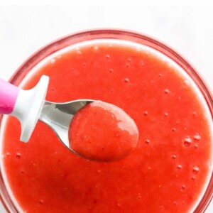 Fresh strawberry puree in a glass bowl. A small spoon is lifting a spoonful out of the bowl.