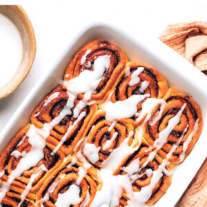 Baking dish with vegan cinnamon rolls topped with icing.