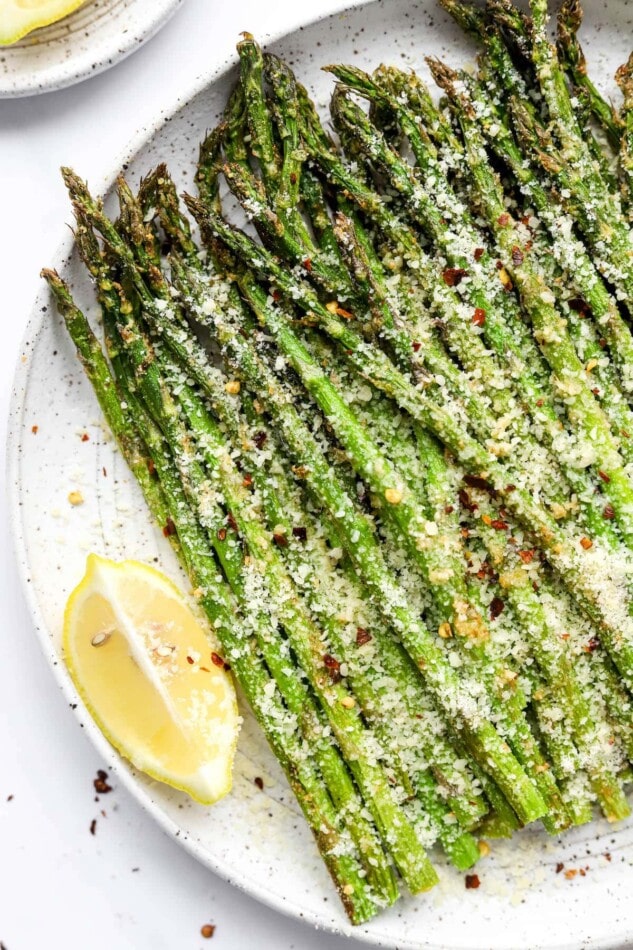 A plate with air fryer asparagus topped with extra cheese, red pepper flakes and a lemon wedge.