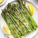 A plate with asparagus and lemon wedges topped with cheese and red pepper flakes.