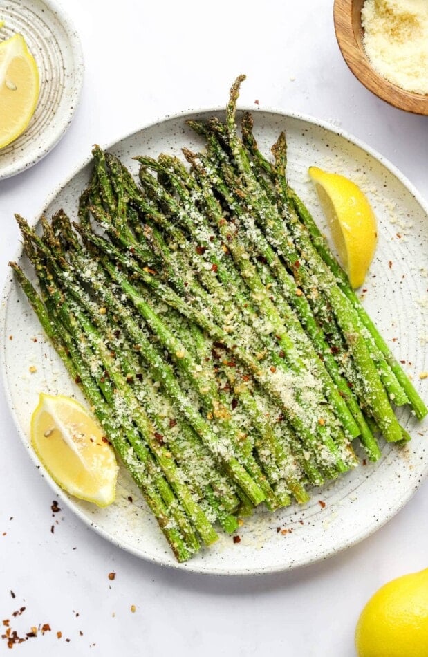 A plate with asparagus and lemon wedges topped with cheese and red pepper flakes.