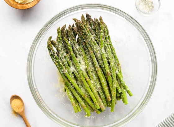 Asparagus in a mixing bowl, tossed with olive oil, garlic powder, salt, pepper and parmesan cheese.