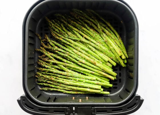 Cooked asparagus spears in an air fryer basket.