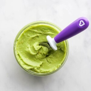 A small jar of avocado puree. A spoon rests in the jar.