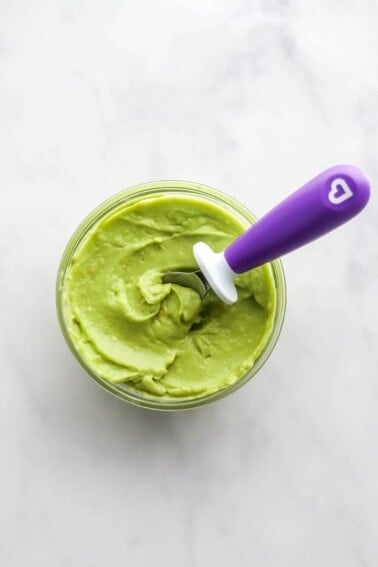 A small jar of avocado puree. A spoon rests in the jar.