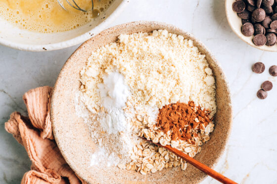 A medium sized bowl with oat flour, almond flour, rolled oats, baking soda, baking powder, cinnamon and salt.