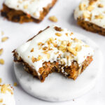 A carrot cake bar topped with vanilla icing. A bite has been taken from the bar.