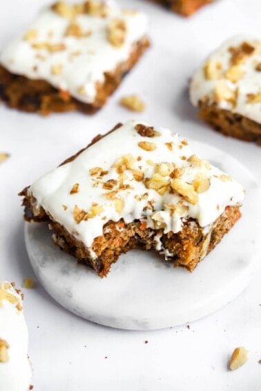 A carrot cake bar topped with vanilla icing. A bite has been taken from the bar.