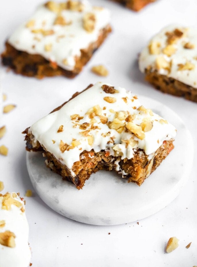 A carrot cake bar topped with vanilla icing. A bite has been taken from the bar.