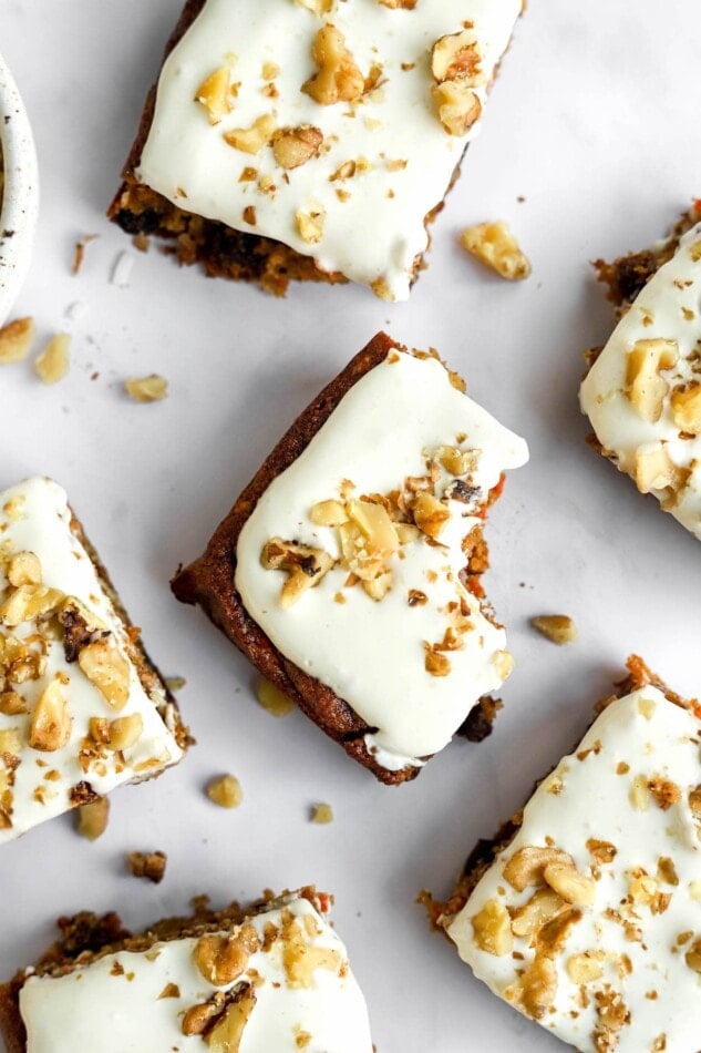 Several squares of carrot cake bars spread around. The center bar has a bite removed.