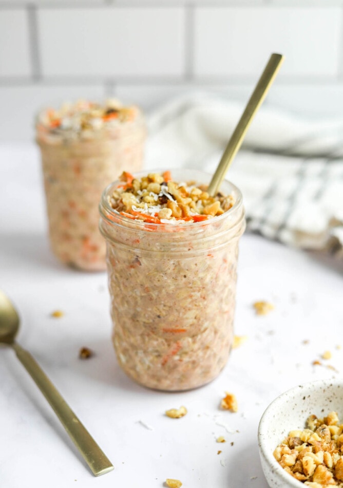 Two jars of carrot cake overnight oats. A spoon is sticking out of one of the jars.