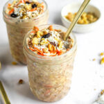 Two jars of carrot cake overnight oats. A spoon is sticking out of the front jar.