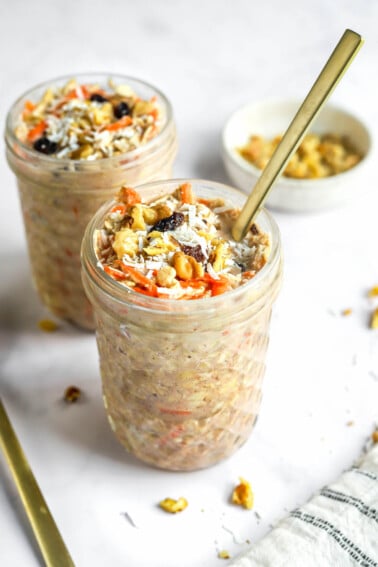 Two jars of carrot cake overnight oats. A spoon is sticking out of the front jar.