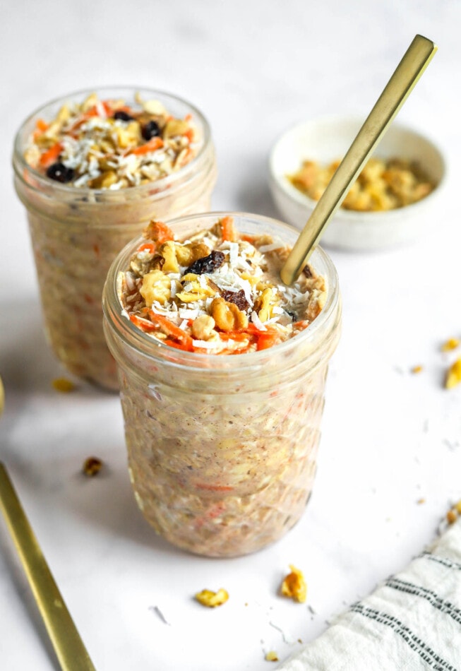 Two jars of carrot cake overnight oats. A spoon is sticking out of the front jar.