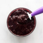 A bowl of blueberry puree with a purple spoon resting in the bowl.