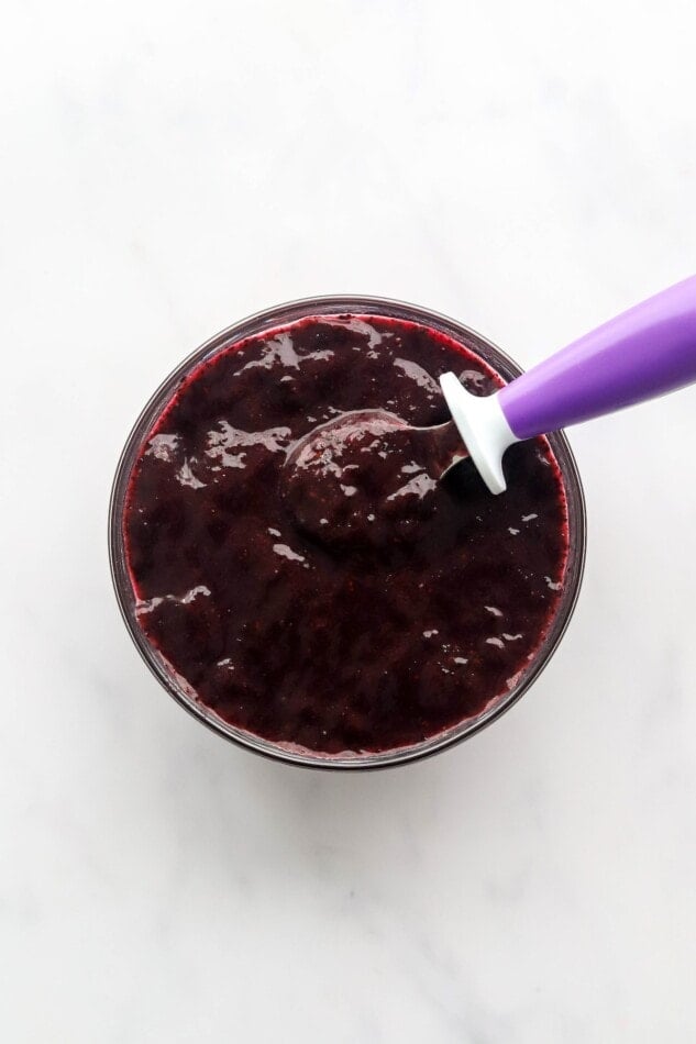 A bowl of blueberry puree with a purple spoon resting in the bowl.