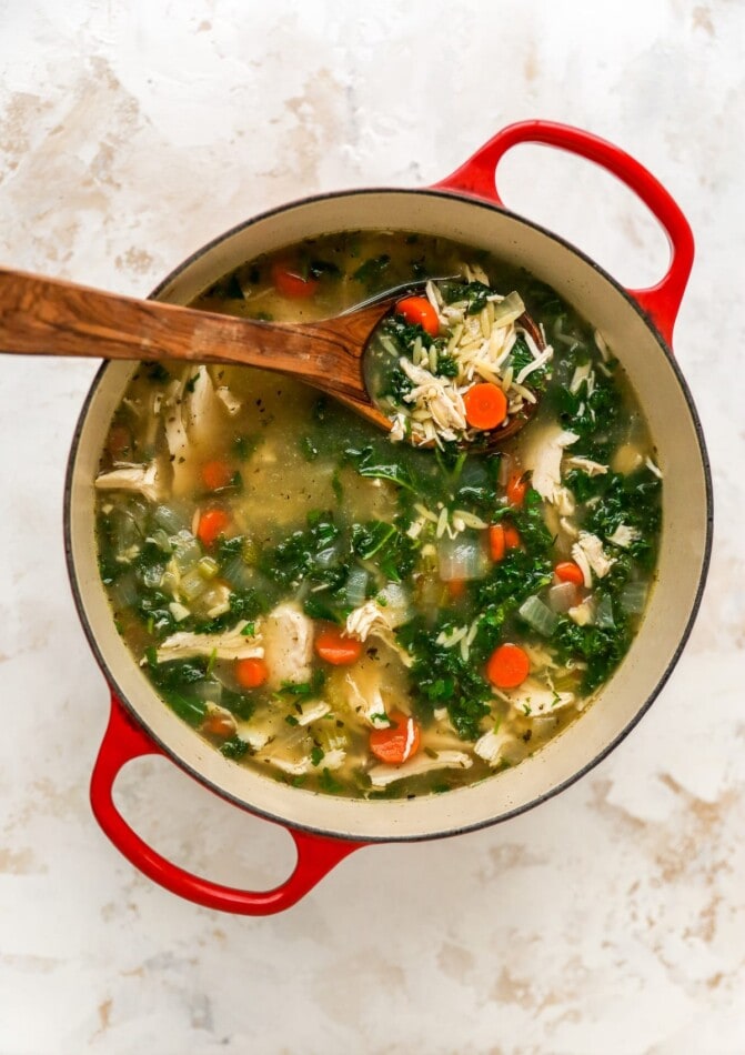 A large pot with lemon chicken orzo soup. A serving spoon rests in the pot.