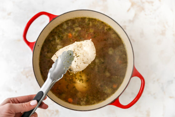 Removing cooked chicken breasts from Dutch oven.