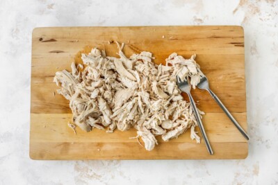 Shredding chicken breasts on a cutting board.