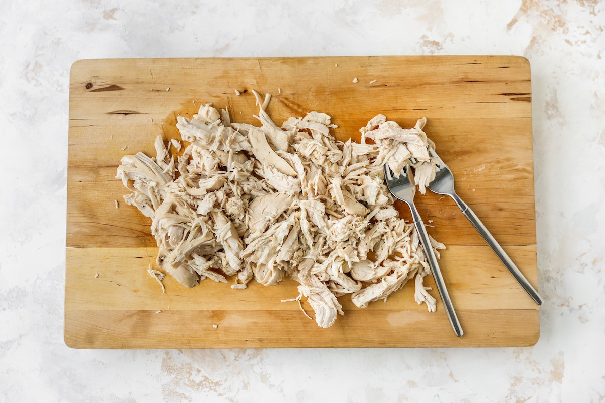 Shredding chicken breasts on a cutting board.
