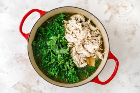 Adding shredded chicken and kale to Dutch oven.