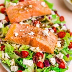 A serving platter with mediterranean salad topped with two filets of salmon.