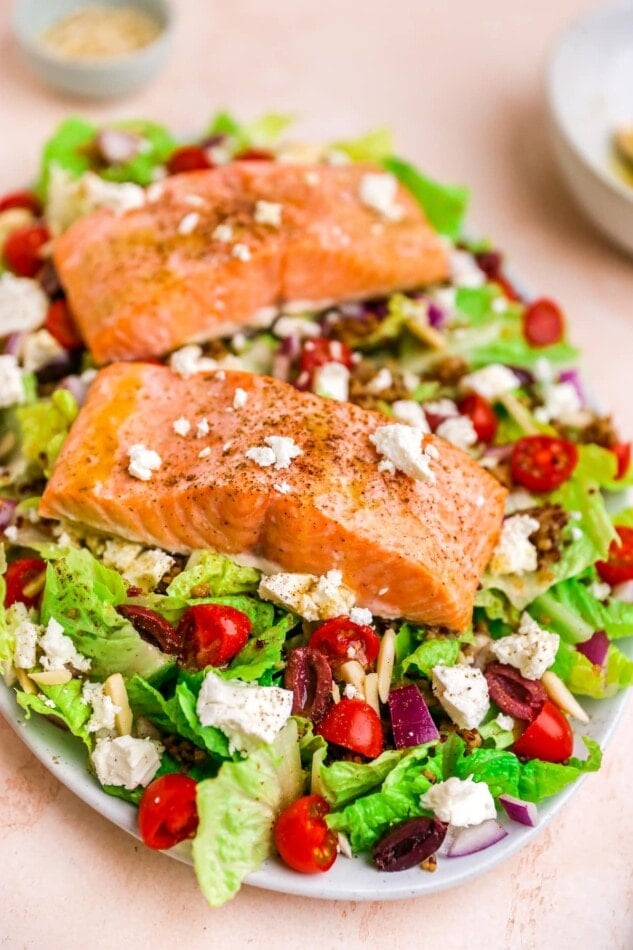 A serving platter with mediterranean salad topped with two filets of salmon.