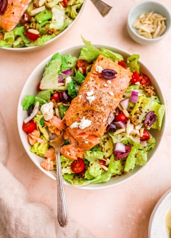 A bowl with mediterranean salad topped with a filet of salmon.