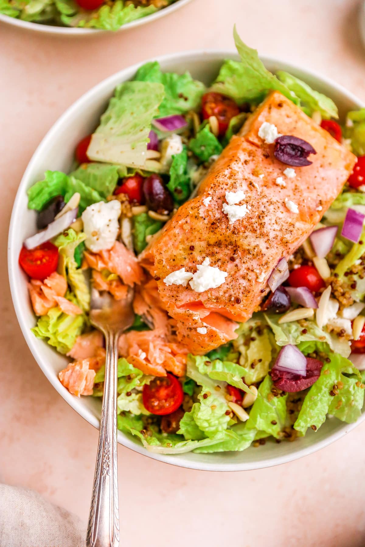 A bowl with mediterranean salad topped with a filet of salmon.