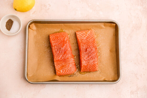Two salmon filets on a parchment lined baking sheet.