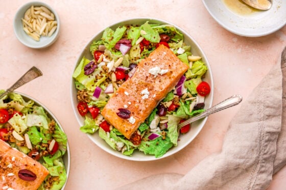 A bowl of mediterranean salad topped with a salmon filet.