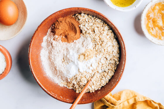 A mixing bowl containing flour, rolled oats, baking soda, baking powder, salt, cinnamon and ground ginger.