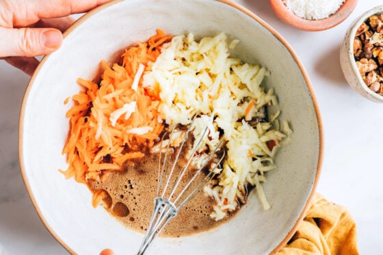 A mixing bowl containing eggs, coconut sugar, applesauce, avocado oil, vanilla extract, grated apples and grated carrots.