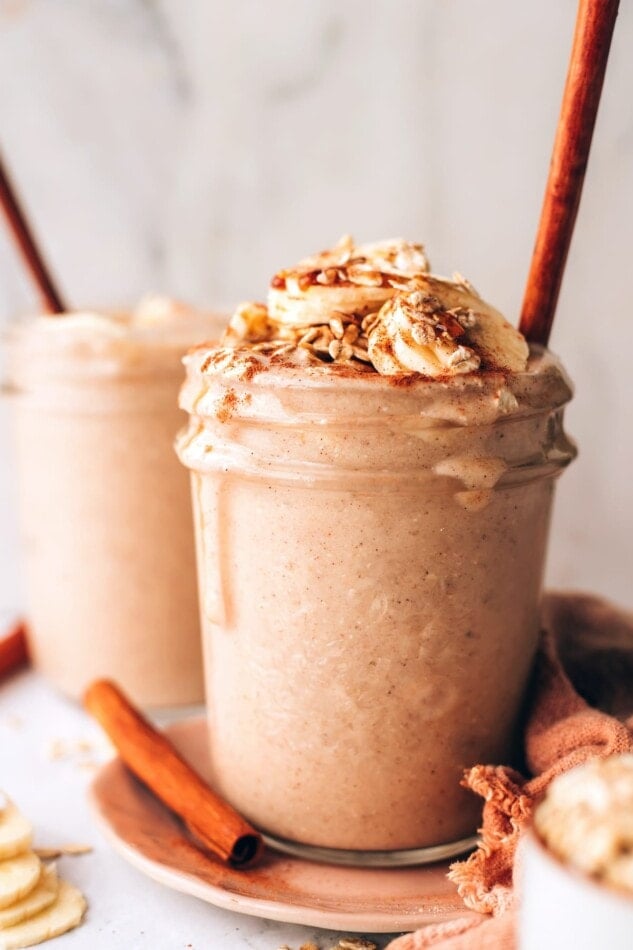 A mason jar containing an oatmeal smoothie. A cinnamon stick pokes out of the top of the smoothie.