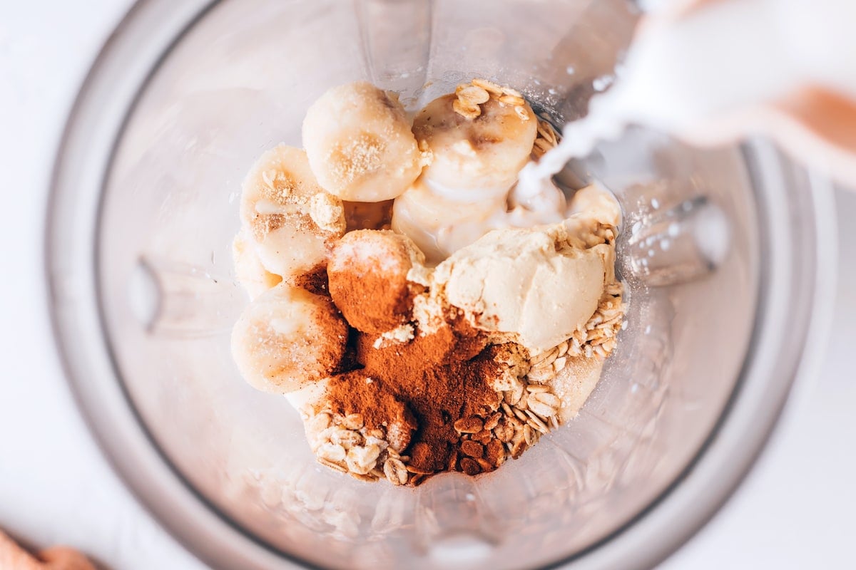 Banana, milk, oats, protein powder, cinnamon, and vanilla in a blender.