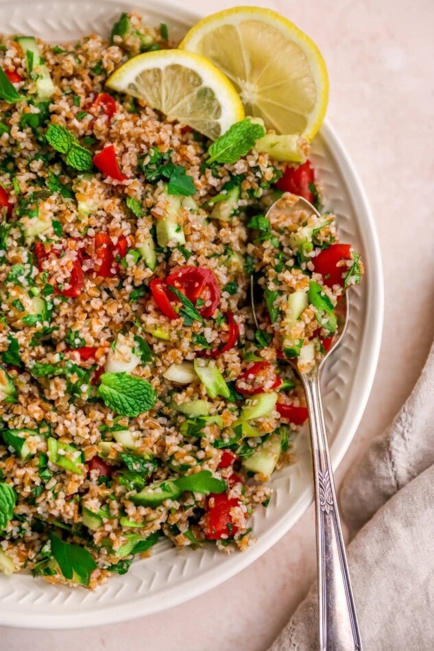 A serving platter containing tabbouleh salad. There is a spoon resting on the platter with lemon slices.