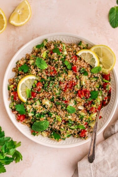 A serving platter with tabbouleh salad topped with fresh mint and lemon slices. A spoon rests on the platter.