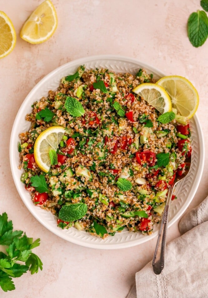 A serving platter with tabbouleh salad topped with fresh mint and lemon slices. A spoon rests on the platter.
