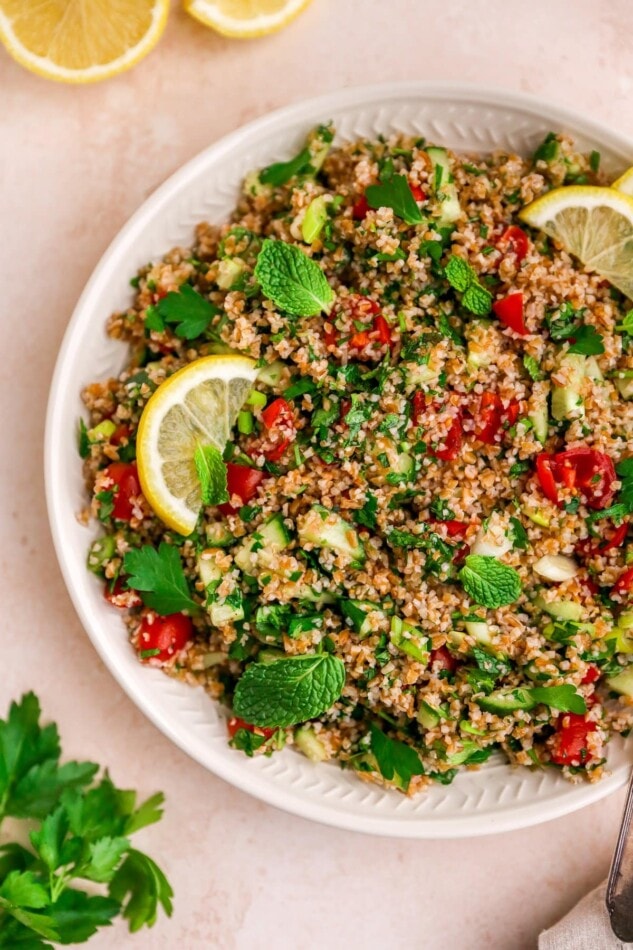 A serving platter with tabbouleh salad topped with fresh mint and lemon slices.