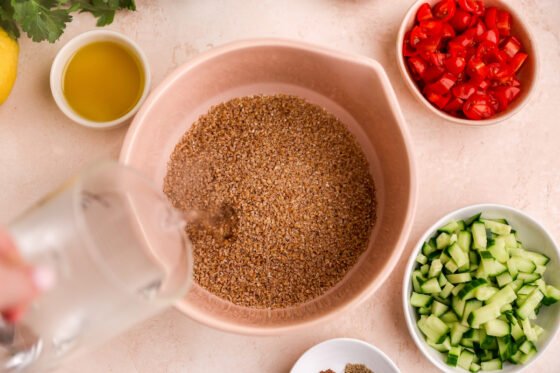 Adding boiling water into a bowl containing bulgur wheat.