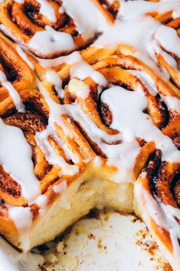 A close up of vegan cinnamon rolls in a baking dish. A roll has been removed.