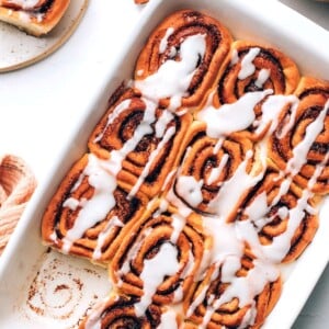 An overhead photo of vegan cinnamon rolls in a baking dish. A roll has been removed from a corner.