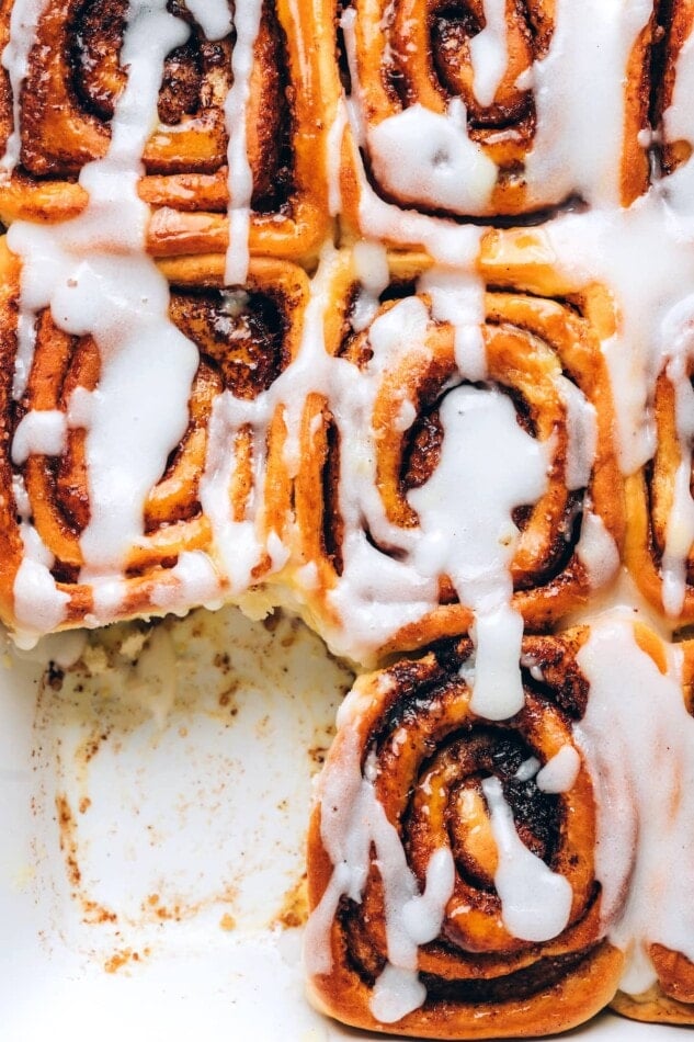 Overhead view of a baking dish with vegan cinnamon rolls topped with glaze. A roll has been removed from a corner.