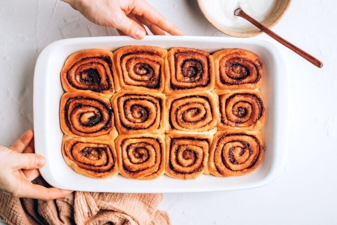 Twelve baked vegan cinnamon rolls in a baking dish.