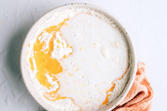 A mixing bowl containing flour, salt and sugar. The yeast mixture and melted vegan butter have been added to the bowl.