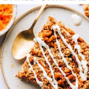 A slice of carrot cake baked oatmeal on a plate. The slice has been drizzled with a maple cream cheese glaze.