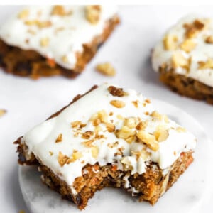 A carrot cake bar topped with vanilla icing. A bite has been taken from the bar.