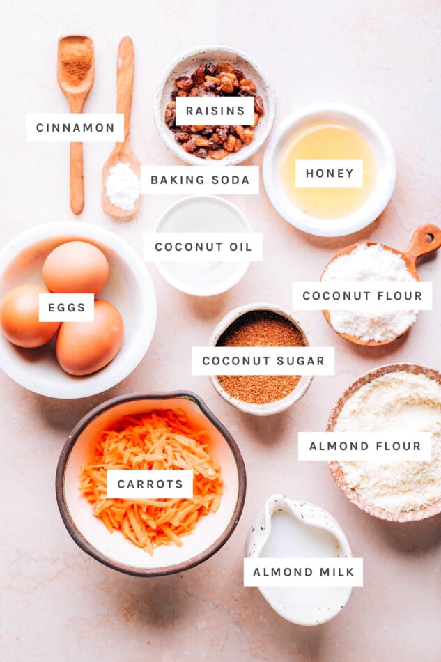 Ingredients measured out to make carrot raisin muffins: cinnamon, raisins, baking soda, honey, coconut oil, coconut flour, coconut sugar, eggs, almond flour, carrots and almond milk.