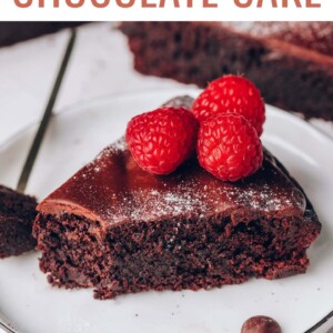 Slice of flourless chocolate cake on a plate. Cake has a bite taken out of it, and is topped with powdered sugar and raspberries.